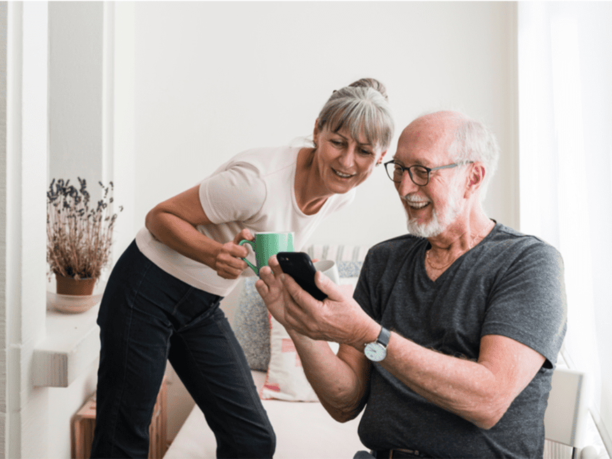 Smiling senior couple looking at a smartphone together while drinking coffee.