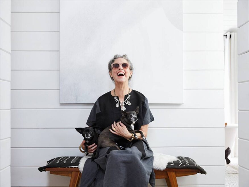 Smiling older woman sitting indoors with two small dogs on her lap.