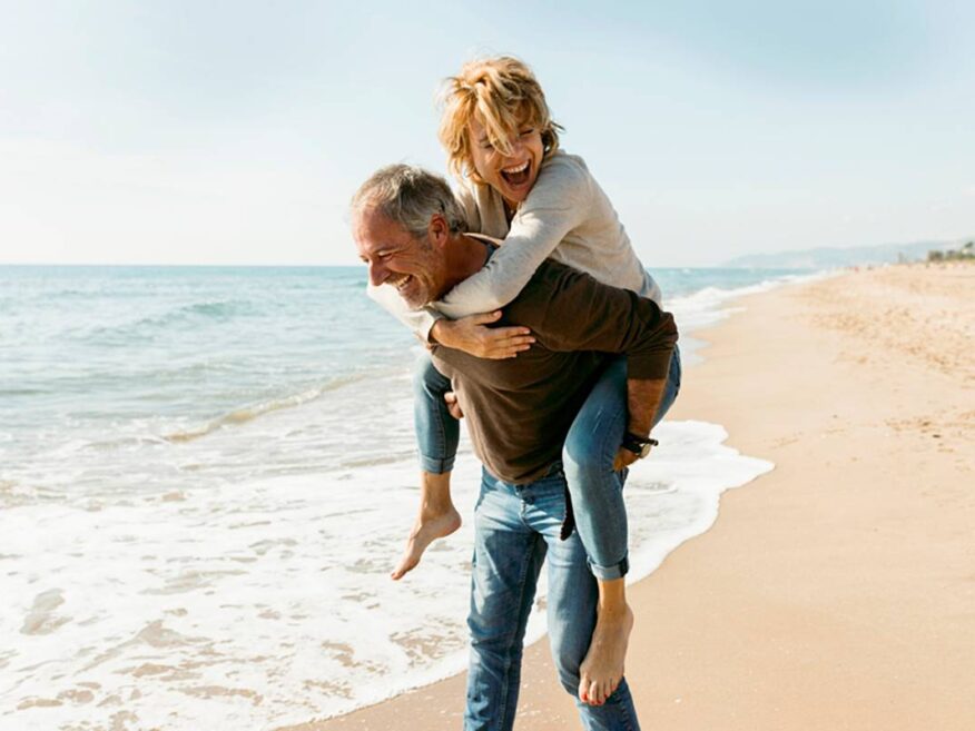 Happy older couple enjoying a piggyback ride while walking along the beach