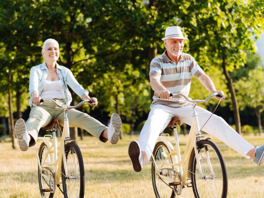 Smiling senior couple riding bicycles together in a park with legs playfully outstretched